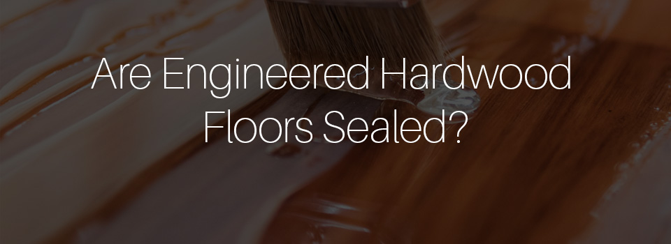 Are Engineered Hardwood Floors Sealed-text on top of a close up image in the background of a hand brush spreading polyurethane on wood flooring