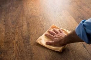A man buffing a hardwood floor with a cloth during routine maintenance